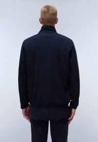 Chaqueta de forro polar azul marino con un alto cuello, mangas largas y un corte relajado, que presenta una textura suave y un hardware mínimo.