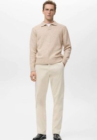 Suéter de punto color beige claro con cuello, combinado con pantalones de pana color crema y zapatos de cuero negros, presentado sobre un fondo neutro.