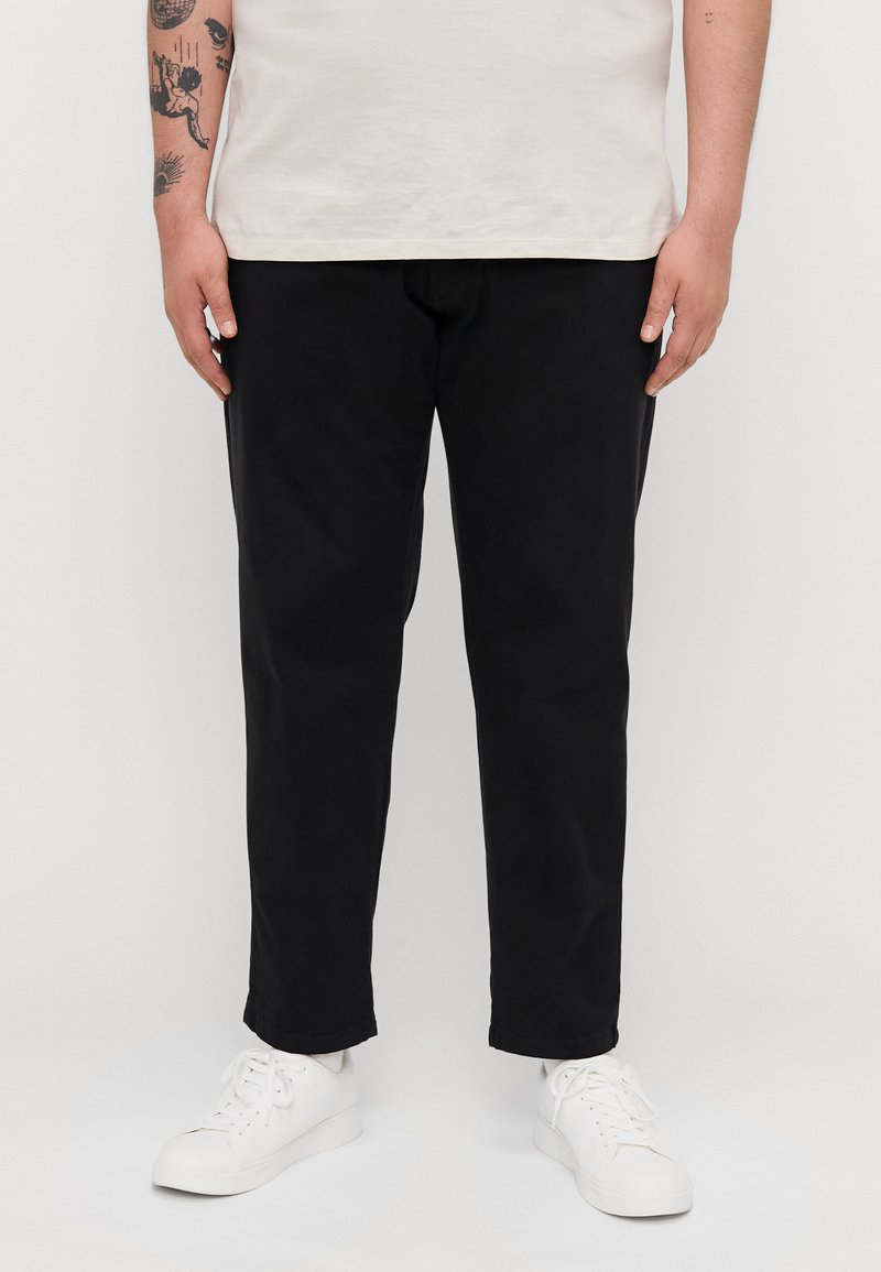 Black cotton trousers with a straight-leg design, featuring a smooth texture and rolled hems, paired with white sneakers.
