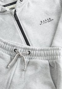 Helehall hall tuukrimütsiga pusa ja dressipüksid, musta tõmblukuga, elastse vöökohaga ja rinnal ning nööril "Baker by Ted Baker" brändinguga.