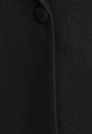 Must have villane segu koht pehme ja tekstureeritud pinnaga; omab ümmargust nööpi ja vertikaalset õmblust. Lihtne, kohandatud disain.