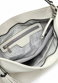 Sac à main en cuir blanc avec un extérieur perforé, des fermetures zippées, et un intérieur gris présentant un motif de texte répétitif. Plusieurs compartiments visibles.