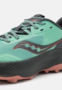 Gros plan sur une chaussure de sport vert menthe et noir avec des lacets à motifs, une tige texturée et une semelle extérieure de couleur corail.