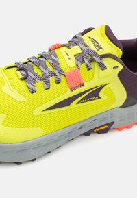 Zapatilla de trail running de un brillante color amarillo con acentos morados, parte superior de malla texturizada, detalles reflectantes y una suela intermedia gris. Cuenta con cordones y una suela exterior de goma.