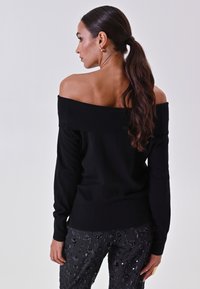 Maglione nero a spalle scoperte con scollatura a costine, maniche aderenti e tessuto testurizzato. Abbinato a pantaloni neri con paillettes.