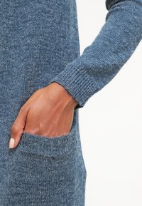 Maglione blu a maglia con polsini a costine e una tasca frontale, che mostra un tessuto morbido e testurizzato con una vestibilità comoda.