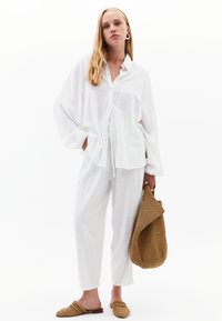 Witte, langarm knoop-overhemd met een relaxte fit, gecombineerd met bijpassende losse broek en een bruine geweven tas. Textuurstof van lichtgewicht.