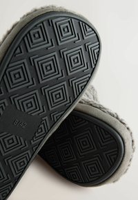 Grå såler med en tekstureret sort gummibund, der har geometriske mønstre. Blødt gråt materiale synligt på kanterne. Størrelse markeret 8/42.