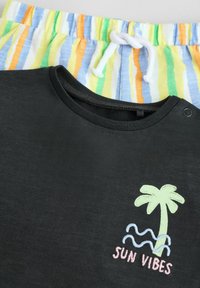 Czarna koszulka z krótkim rękawem z haftem "SUN VIBES" i palmą, połączona z wielokolorowymi, paskowanymi szortami ze sznurkiem w lekkim materiale.