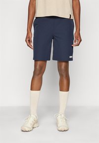 Marineblå sportshorts laget av et lett stoff, med en glatt tekstur og en liten reflekslogo på venstre bein.