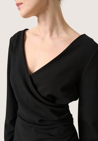 Schwarzes drapiertes Kleid mit langen Ärmeln, das einen V-Ausschnitt und eine glatte Textur aufweist, betont elegante Linien und eine figurbetonte Passform.