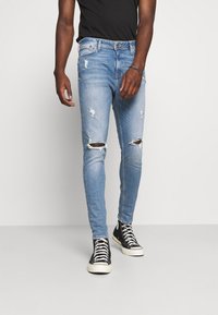 Jean azul claro desgastados con roturas en las rodillas, diseño ajustado y un lavado desvanecido, combinados con zapatillas negras de caña alta.