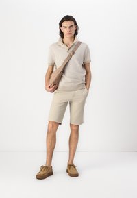Beige stripete polo-skjorte, beige shorts og brune semsket snøresko. Skulderveske i matchende tone, enkel design med justerbar stropp.