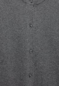 Měkká šedá vlněná tkanina se čtyřmi černými knoflíky rovnoměrně rozmístěnými uprostřed.