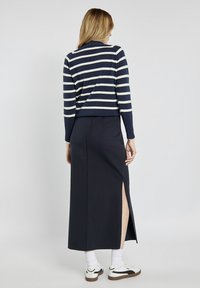 Sweter w niebiesko-białe paski zestawiony z ciemną, długa spódnicą sięgającą ziemi z bocznym rozcięciem. Model ma na sobie białe sneakersy i skarpetki.