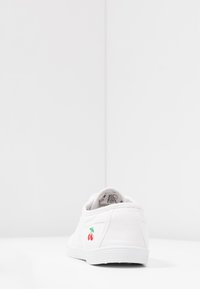 Baskets blanches en toile avec une silhouette basse, dotées d'une broderie de cerises vertes et rouges au talon, d'un matériau texturé et d'une semelle en caoutchouc.