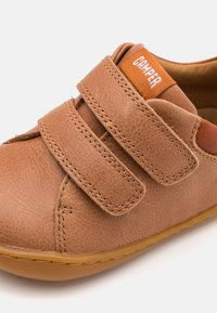 Braune Leder-Schuhe mit Klettverschlüssen, runder Zehenpartie und einem kontrastierenden orangefarbenen Logo-Tag an der Zunge. Flexible Gummisohle erhöht den Komfort.
