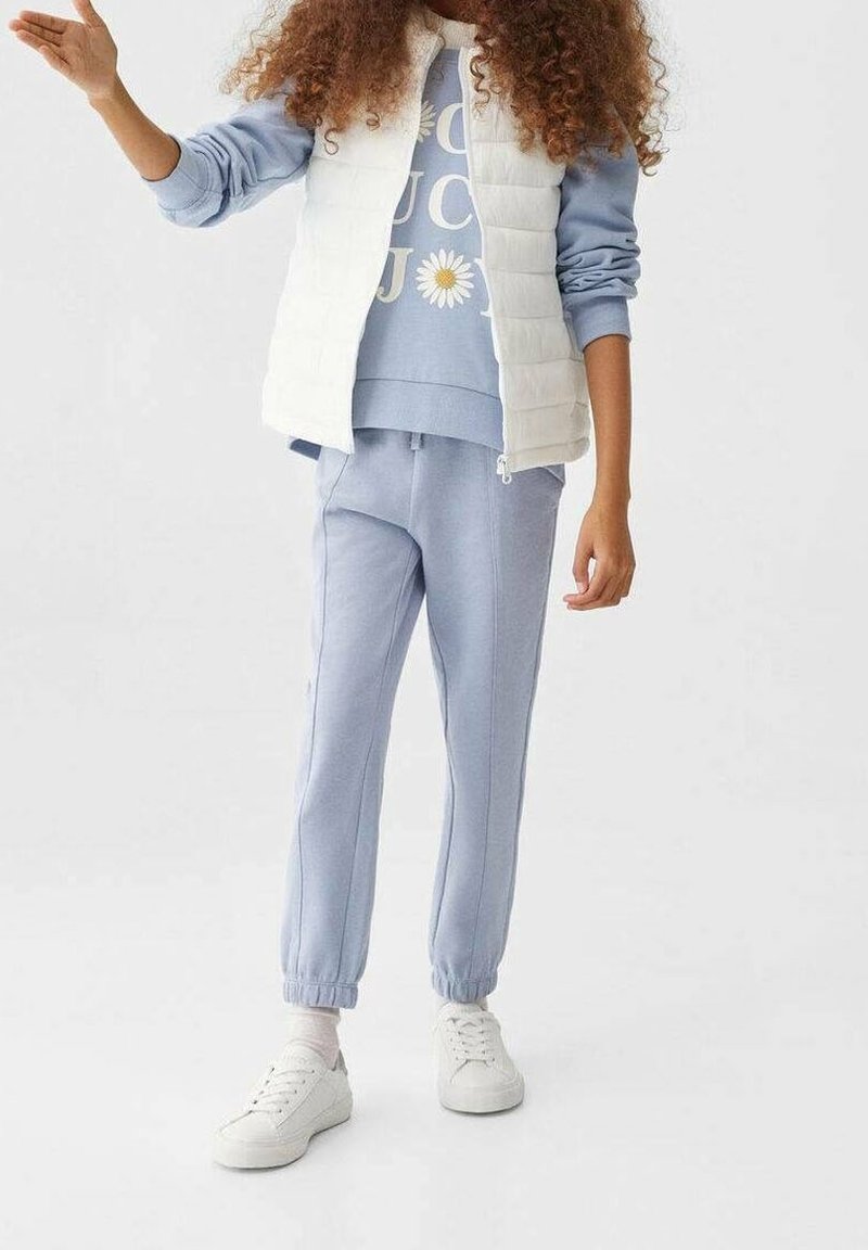 Light blue sweatshirt with a floral graphic, paired with matching joggers and a white padded vest. White sneakers complete the outfit.