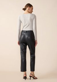 Schwarze Lederhose mit taillierter Passform, sichtbaren Nähten und hoher Taille. Kombiniert mit einem hellgrauen Langarmoberteil und schwarzen Hochzeiten.