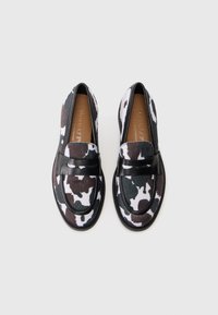 Pair of black and white cow print loafers with black leather strap and tan insoles on white background.