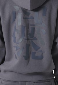 Sudadera con capucha en tejido gris oscuro que presenta un gráfico texturizado en varios tonos de gris, con un corte holgado y puños y bajos acanalados.