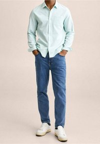 Chemise boutonnée vert menthe clair à manches longues, associée à un jean bleu et des baskets blanches. La chemise possède une poche poitrine et une coupe standard.