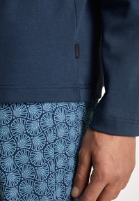 Navy blauwe langewerks bovenstuk met ronde hals en geweven stof. Gecombineerd met geblokte shorts met een blauw-witte cirkelvormige design.