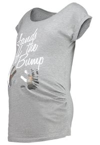 Camiseta de maternidad gris con escote amplio, mangas cortas y detalles fruncidos. En la parte delantera presenta el texto "Manos fuera de la barriga" y gráficos de huellas de manos.