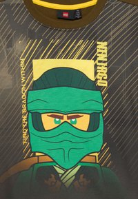 LEGO Ninjago karakter zöld ninja maszkban és öltözetben, "Találd meg a sárkányt magadban" és "Ninjago" felirattal egy sötét csíkozott háttéren.