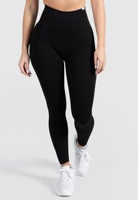 Leggings neri a coste con vita alta e texture liscia, abbinati a sneakers bianche. Nessun motivo o accessorio visibile.