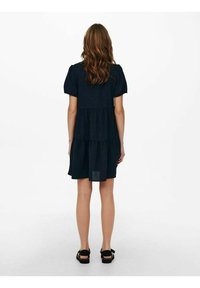 Schwarzes, gestuftes Kleid mit kurzen Puffärmeln, aus leichtem Stoff gefertigt, mit einem lockeren Schnitt und einem Saum, der bis zur Mitte des Oberschenkels reicht.