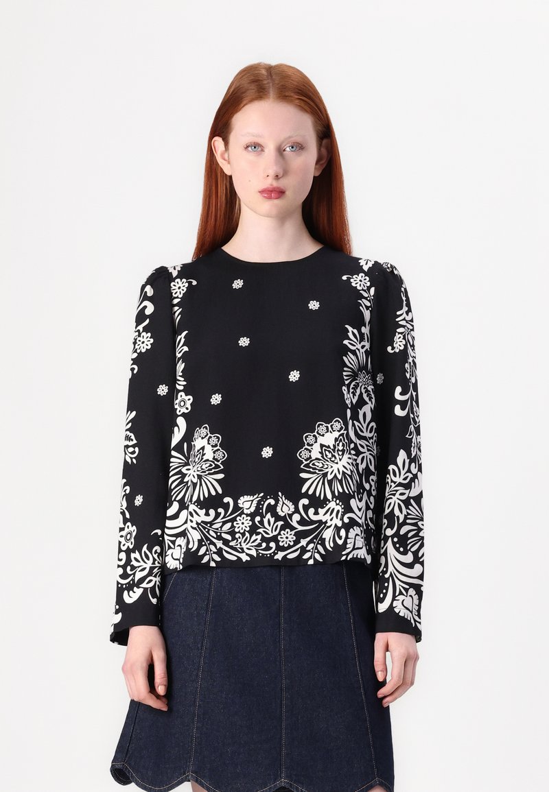 Schwarzes Langarmshirt mit weißen Blumen- und abstrakten Mustern, ausgestattet mit einem runden Ausschnitt und einer lockeren Passform, kombiniert mit einem Jeansrock.
