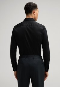 Zwarte langemouwen shirt met een standaard kraag, gladde textuur en knoopmanchetten, gecombineerd met donkere, gestreepte broek en een aansluitende tailleband.