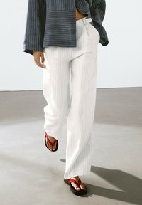 White pinstriped wide-leg pants paired with a blue striped jacket and red flip-flops, highlighted on a neutral floor.