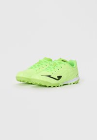 Par de zapatillas deportivas de césped en neón verde con logo y cordones negros sobre un fondo blanco, angulados ligeramente hacia la derecha.