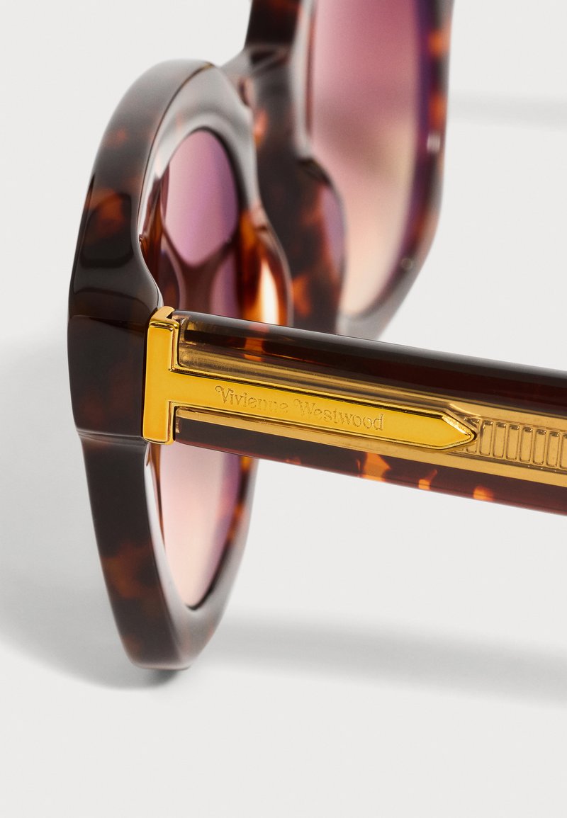 Runde Schildpatt-Sonnenbrille mit violetten Gläsern und einem goldfarbenen Metallbügel mit eingraviertem Vivienne Westwood-Logo.