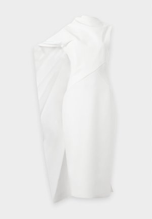 Femme aux longs cheveux foncés portant une robe midi blanche sans manches avec un tissu drapé asymétrique et des talons beiges à bride à la cheville.