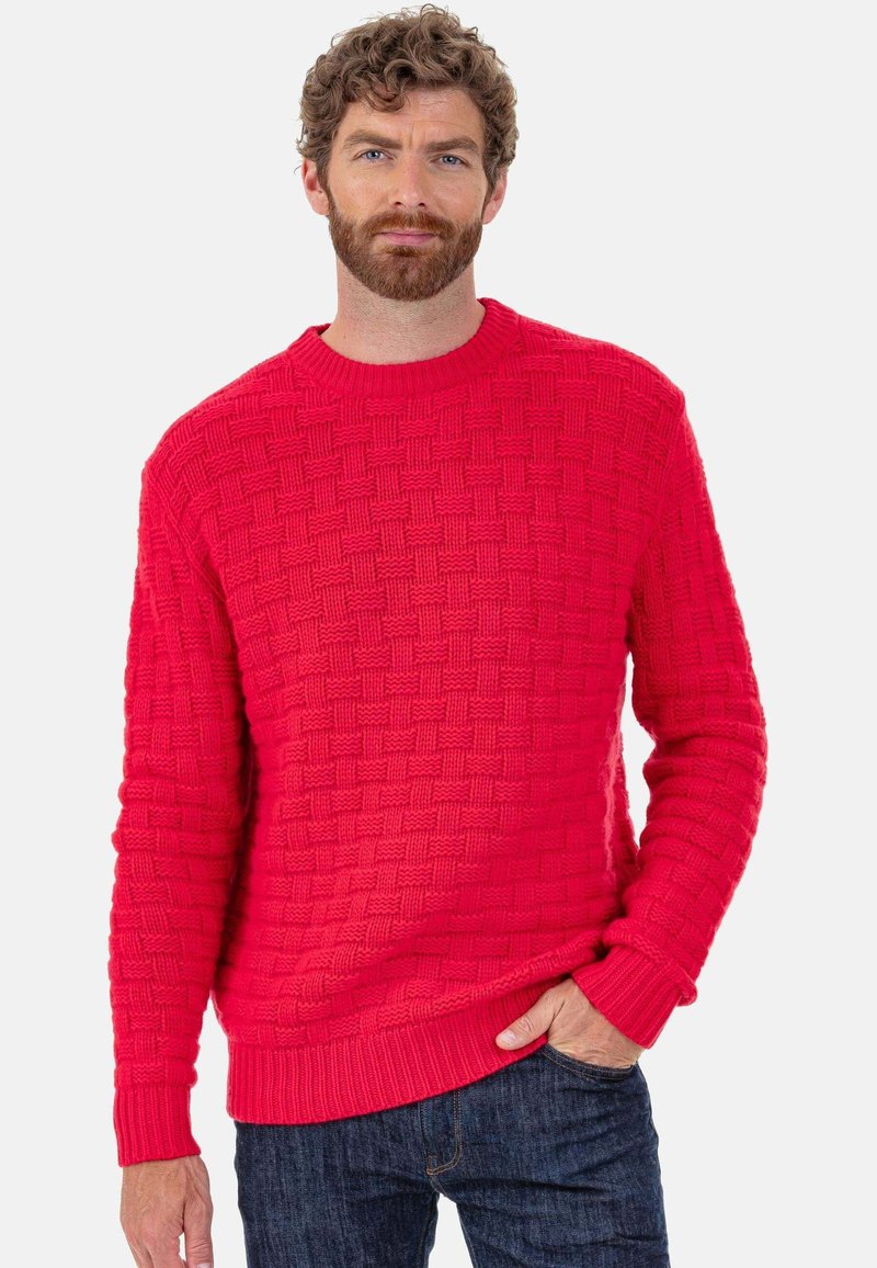 Pull en maille rouge avec un motif texturé tissé. Il présente un col rond, des poignets et un ourlet côtelés, associé à un jean denim foncé.