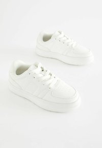 Baskets blanches avec une tige en cuir, bout rond, semelle en caoutchouc plate et fermeture à lacets. Comprend des accents cousus et des perforations.