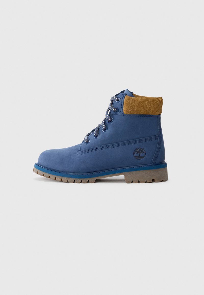 Bota de cuero azul con cordones, con un cuello acolchado marrón, suela de goma gruesa y con un grabado de la marca en el lado.