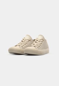 Zapatillas de lona beige con puntera redonda, parte superior texturizada y cordones planos. Presentan una suela de goma con un ligero relieve para mayor agarre. Diseño minimalista.