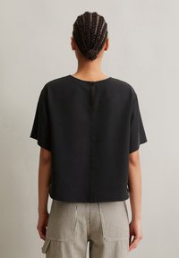 Top nero a maniche corte con scollatura tonda e chiusura con bottone sul retro. Realizzato in un tessuto morbido, presenta una vestibilità rilassata e orlo dritto.