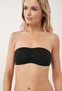 Melna strapless bikini augšdaļa, izgatavota no struktūrēta materiāla, ar saniegtu priekšpusi un bezšuvju malām, nodrošinot gludu siluetu.