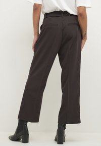 Bruine wijde broek met een hoge taille, voorzien van twee achterzakken en een soepele textuur. Gedragen met zwarte enkellaarzen.
