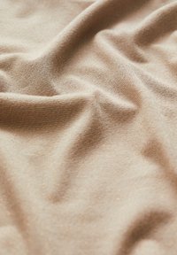 Světlý béžový materiál s jemnou, texturovanou vazbou a subtilními zlatými tečkami, zavěšený tak, aby ukázal záhyby a sklady.