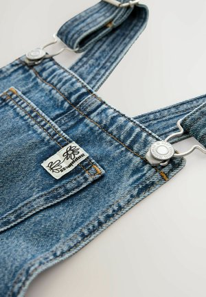 Denim overalls with adjustable straps, light blue color, metal clasps, contrasting stitching, and a label featuring a flower design.