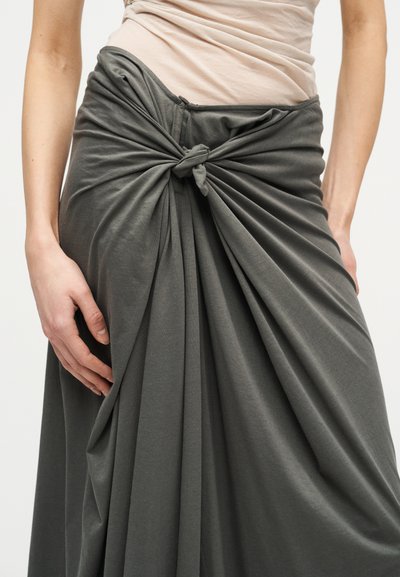 Γυναίκα που φοράει μια ανοιχτή γκρι φούστα, ριχτή και δεμένη σε κόμπο στη μέση, συνδυασμένη με ένα εφαρμοστό ανοιχτό μπεζ τοπ.