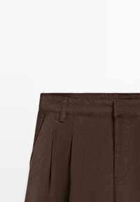 Pantalon marron taille haute avec passants de ceinture, plis à l'avant et poches latérales sur fond blanc.