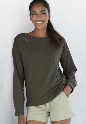 Olivgrünes Langarmoberteil mit gerafften Bündchen und "Bench."-Logo am Ausschnitt, kombiniert mit hellolivgrünen Shorts mit seitlichen Taschen.