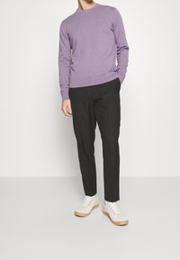Pull violet à manches longues avec un col rond et un petit logo, associé à un pantalon noir ajusté et des baskets blanches à semelle marron clair.